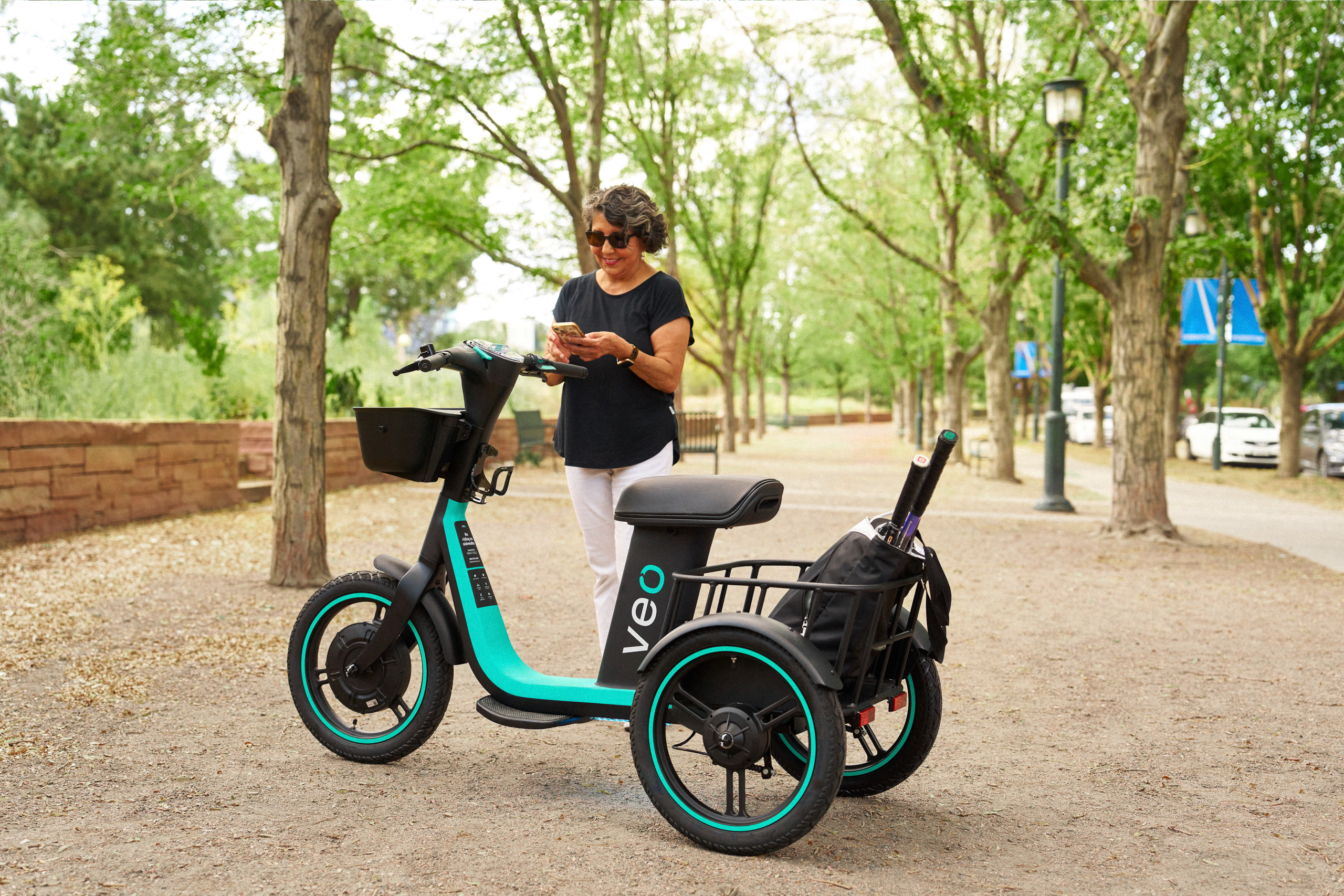 Woman stands behind the trike, about to unlock it with her phone.